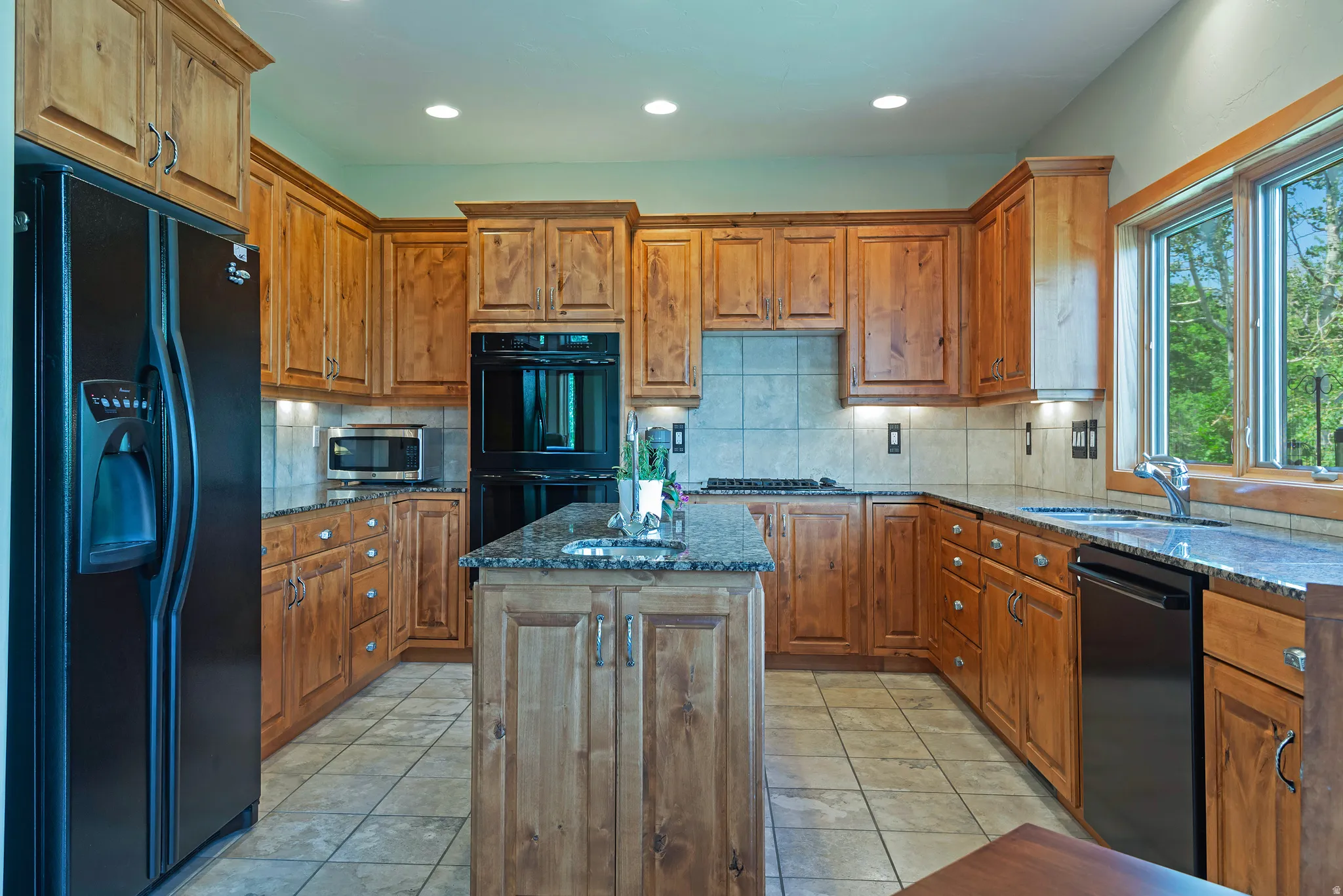 Kitchen featuring wood cabinetry, dark countertops, built-in appliances, a central island, and tile flooring