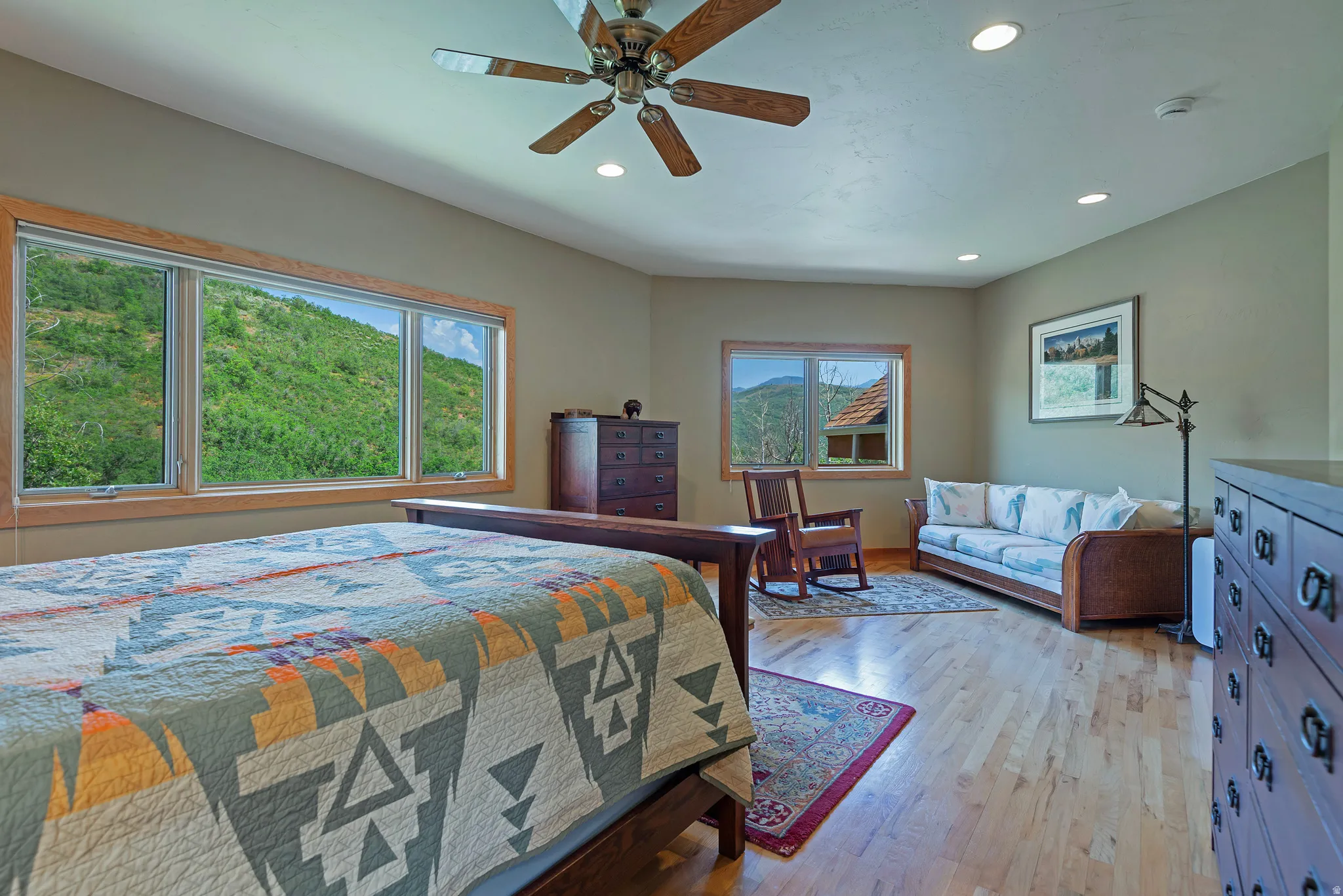 Spacious room featuring multiple windows with natural wood trim, wood-finish flooring, a ceiling fan with integrated lighting, and recessed ceiling lights