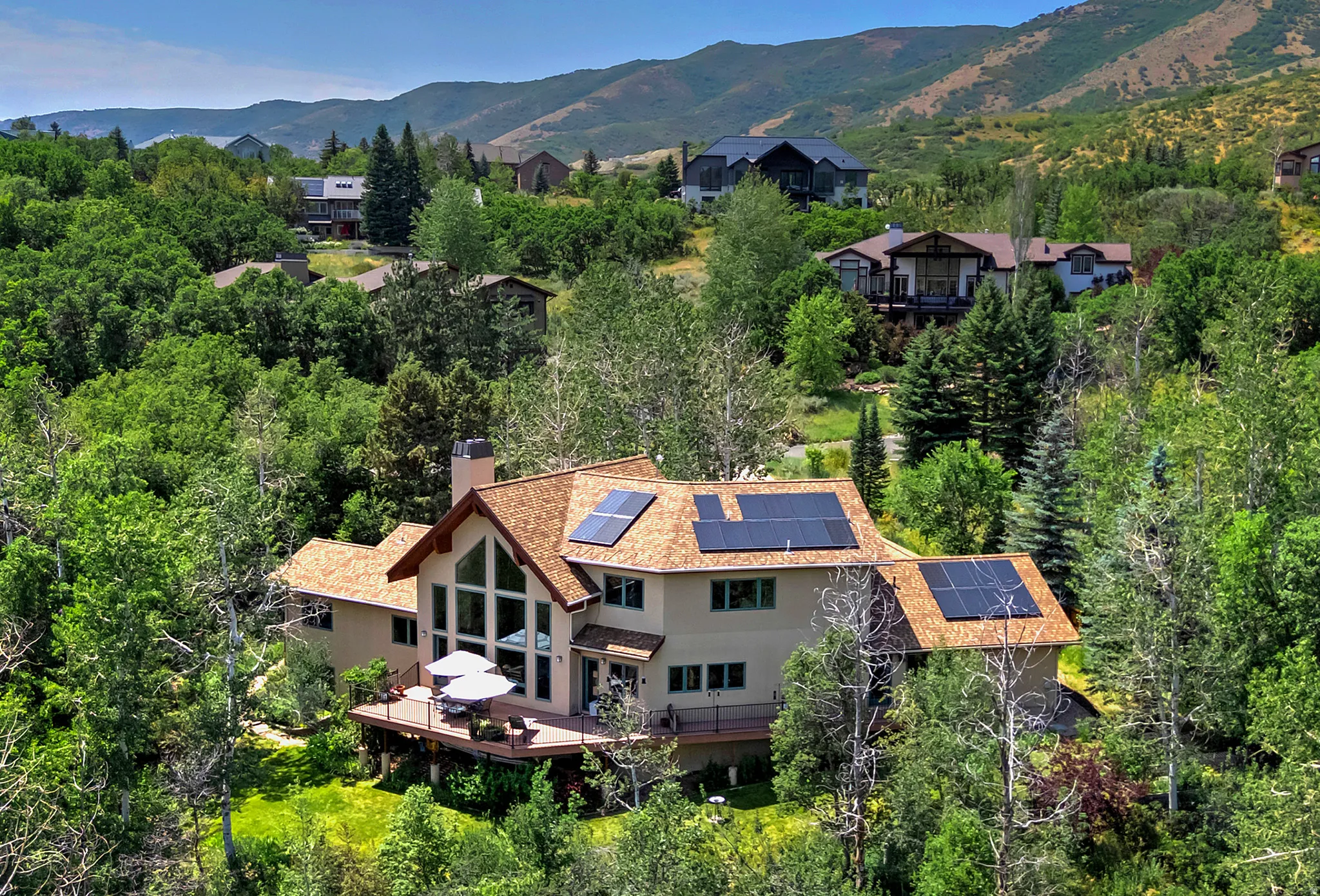 Contemporary residence featuring a prominent gabled roofline with integrated solar panels, a multi-level wood deck, and an expansive window wall