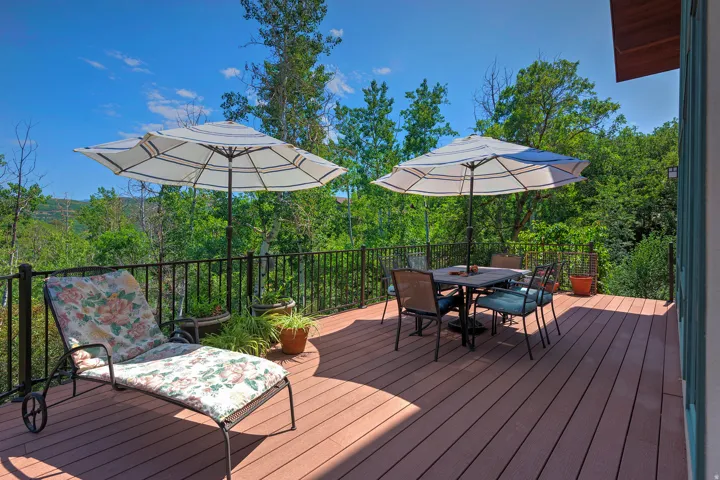 Spacious outdoor deck featuring wood-finish flooring, black metal railing, and lush surrounding greenery