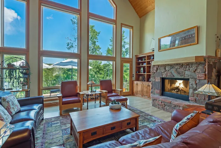 Spacious living area featuring a stone-clad fireplace with wood mantle, vaulted ceilings with wood-finish paneling, and wood-finish flooring