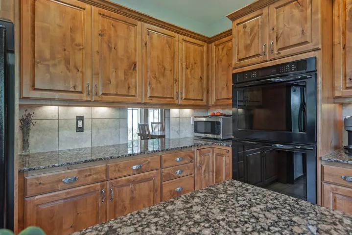 Built-in double oven within a kitchen featuring wood cabinetry, granite countertops, and a tiled backsplash