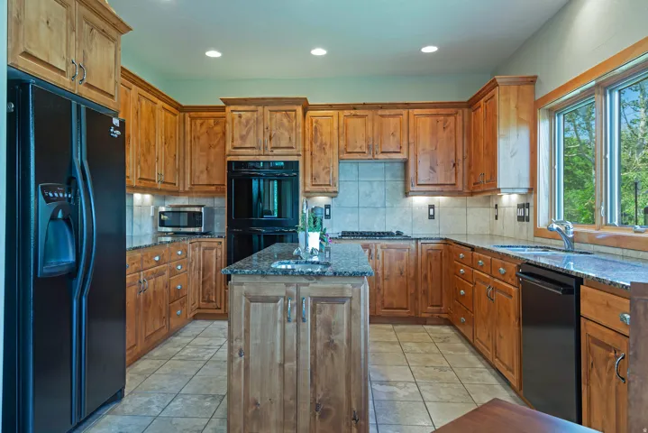 Kitchen featuring wood cabinetry, dark countertops, built-in appliances, a central island, and tile flooring