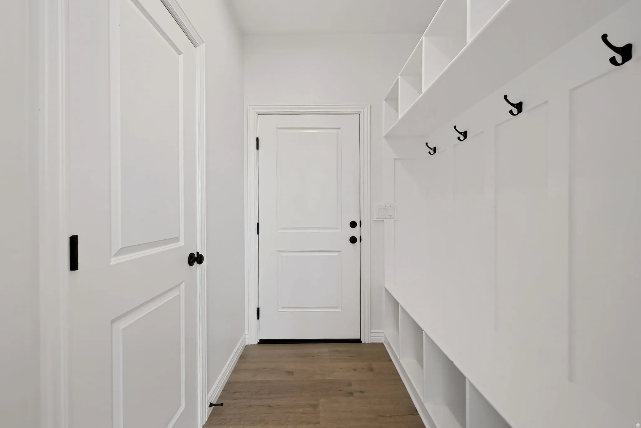 Mudroom featuring wood-finish flooring, white built-in cubbies, coat hooks, and white paneled doors with matte black hardware
