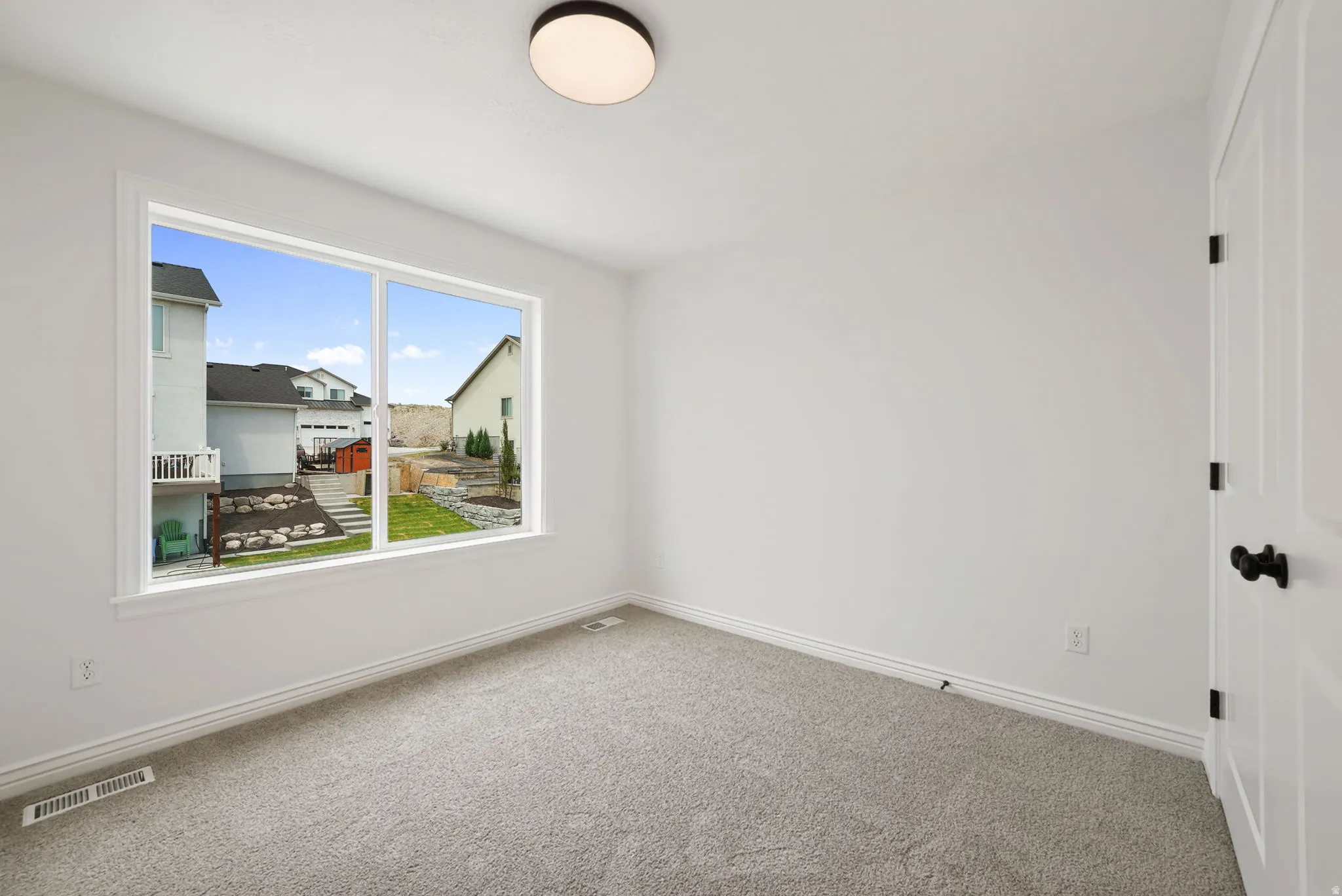 Room featuring a large window, neutral carpet, white walls, and a ceiling-mounted light fixture