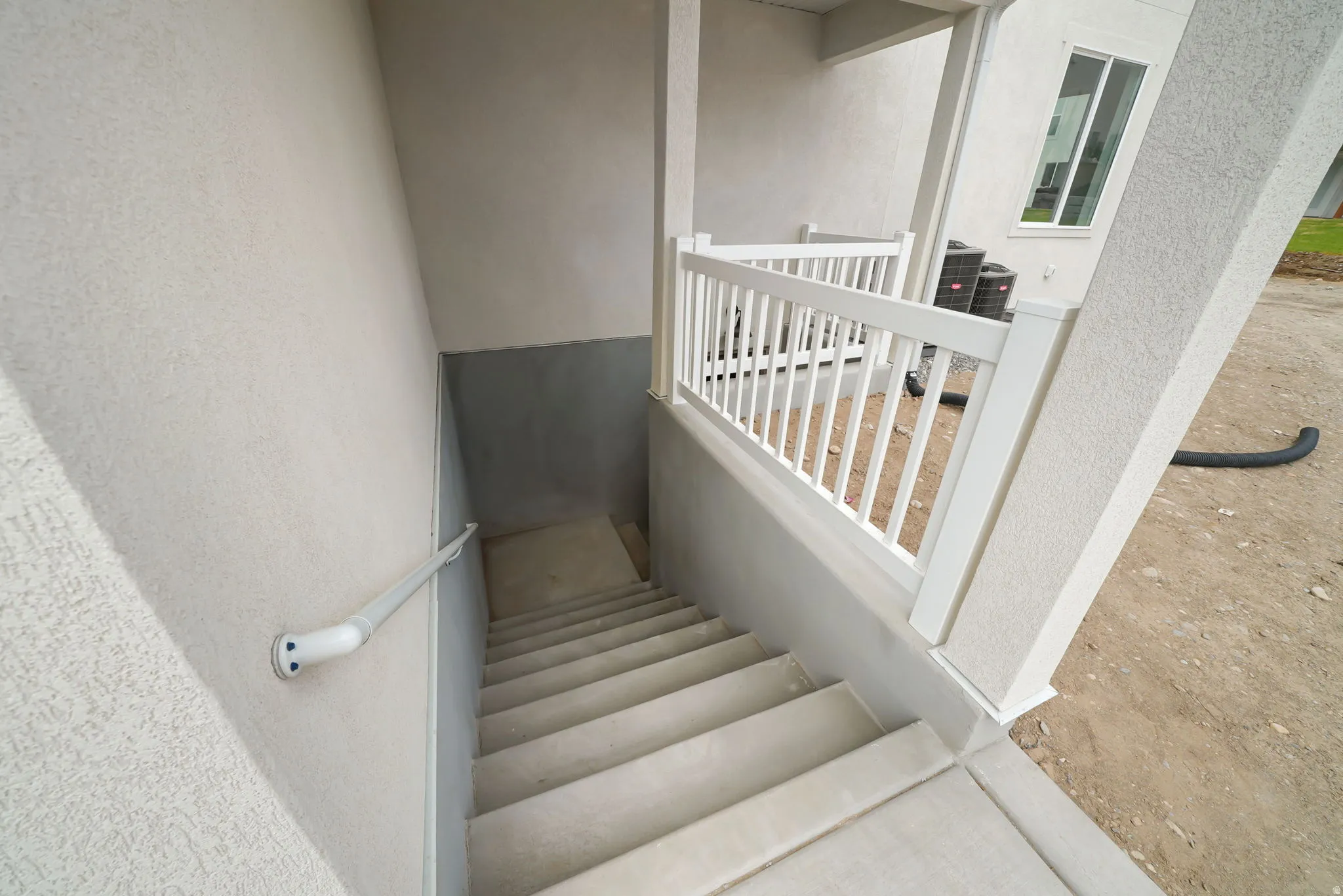Exterior staircase featuring concrete steps and a white wall-mounted handrail