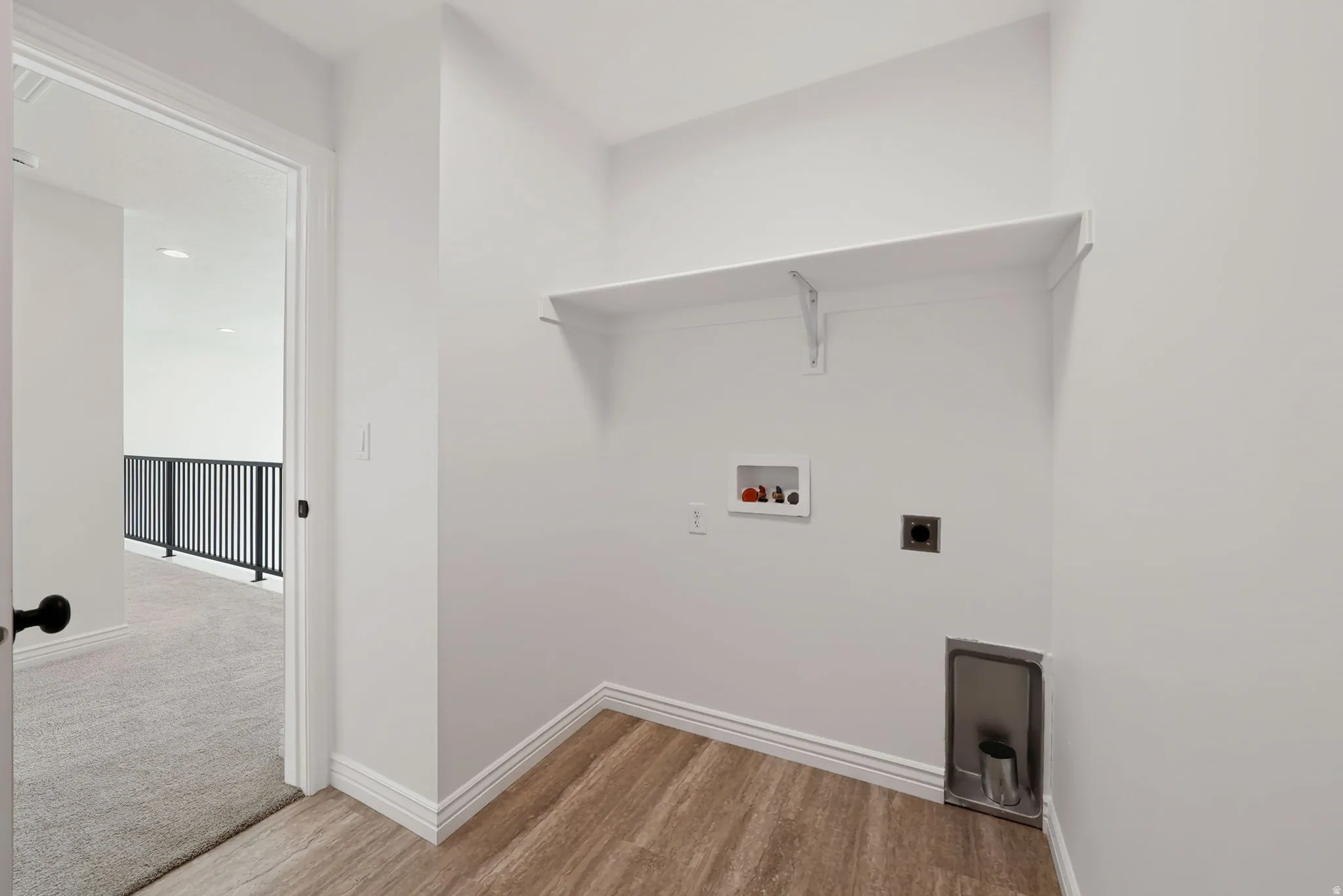 Dedicated laundry area with wood-finish flooring, white wall shelving, and utility hookups