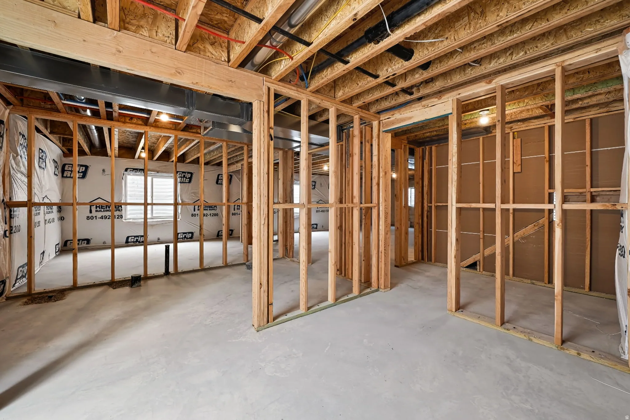 Unfinished basement featuring wood framing, exposed ceiling joists, concrete flooring, and multiple window openings