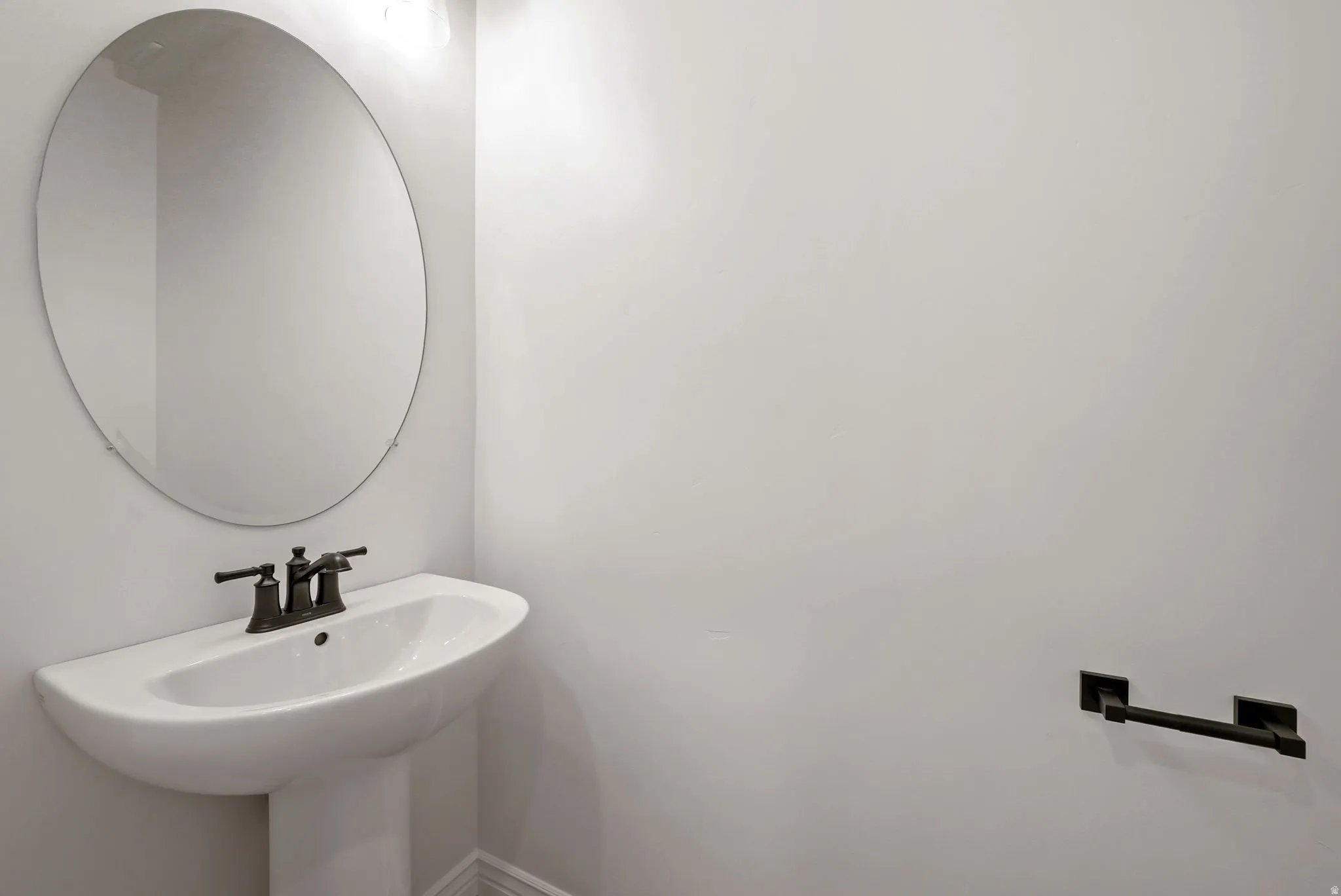 Pedestal sink with dark-finished faucet and large oval mirror