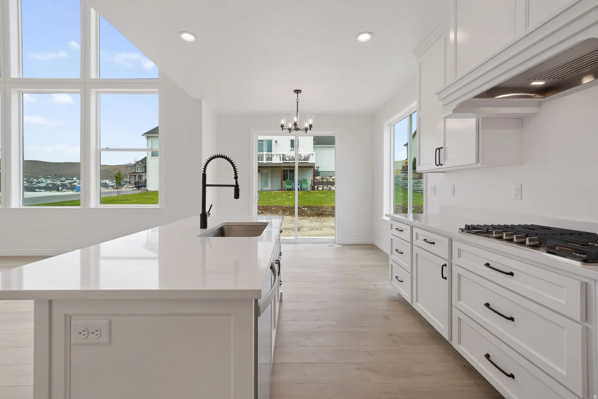 Modern kitchen featuring an expansive island with an undermount sink and matte black faucet, surrounded by white cabinetry with dark hardware