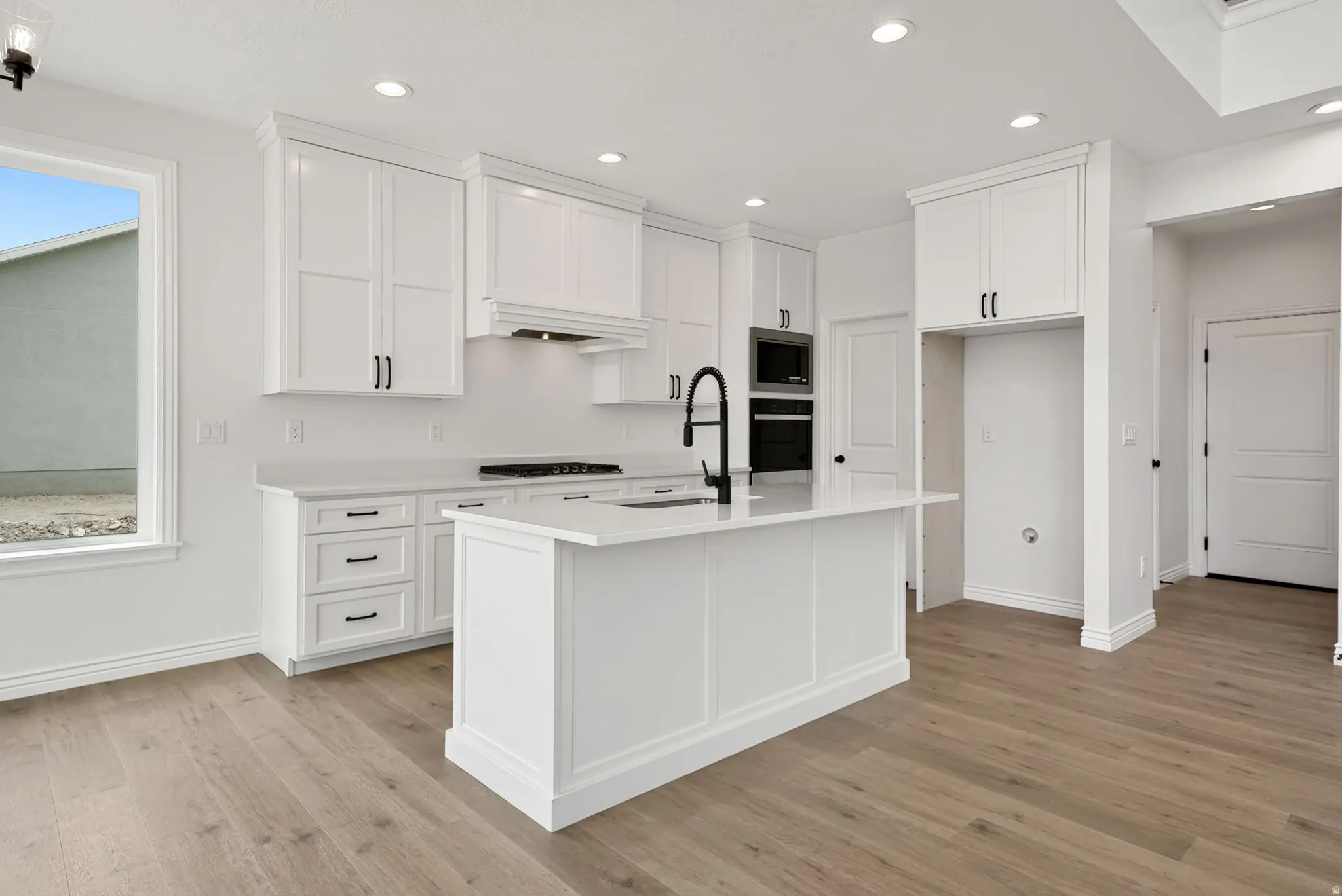 Modern kitchen featuring white shaker cabinetry, an island with an integrated sink and matte black faucet, recessed lighting, and wood-finish flooring