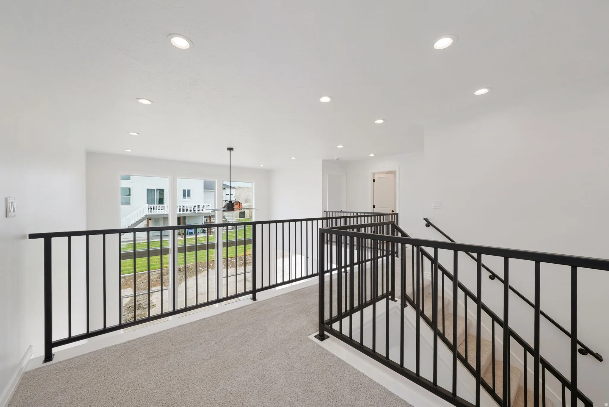 Open upper landing featuring light gray carpeting, contemporary black metal railings, recessed lighting, and expansive windows