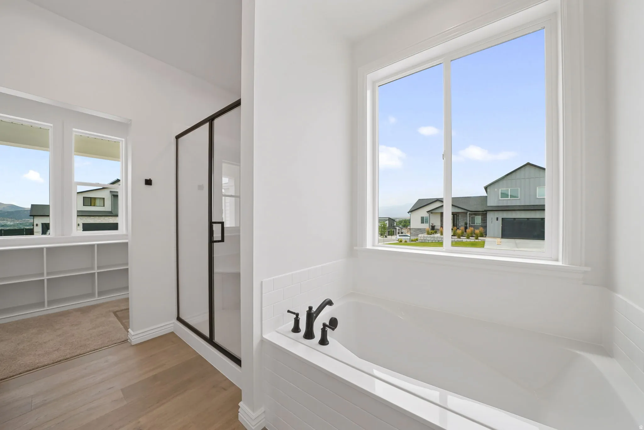 White soaking tub with matte black fixtures, set against a tiled surround and large window