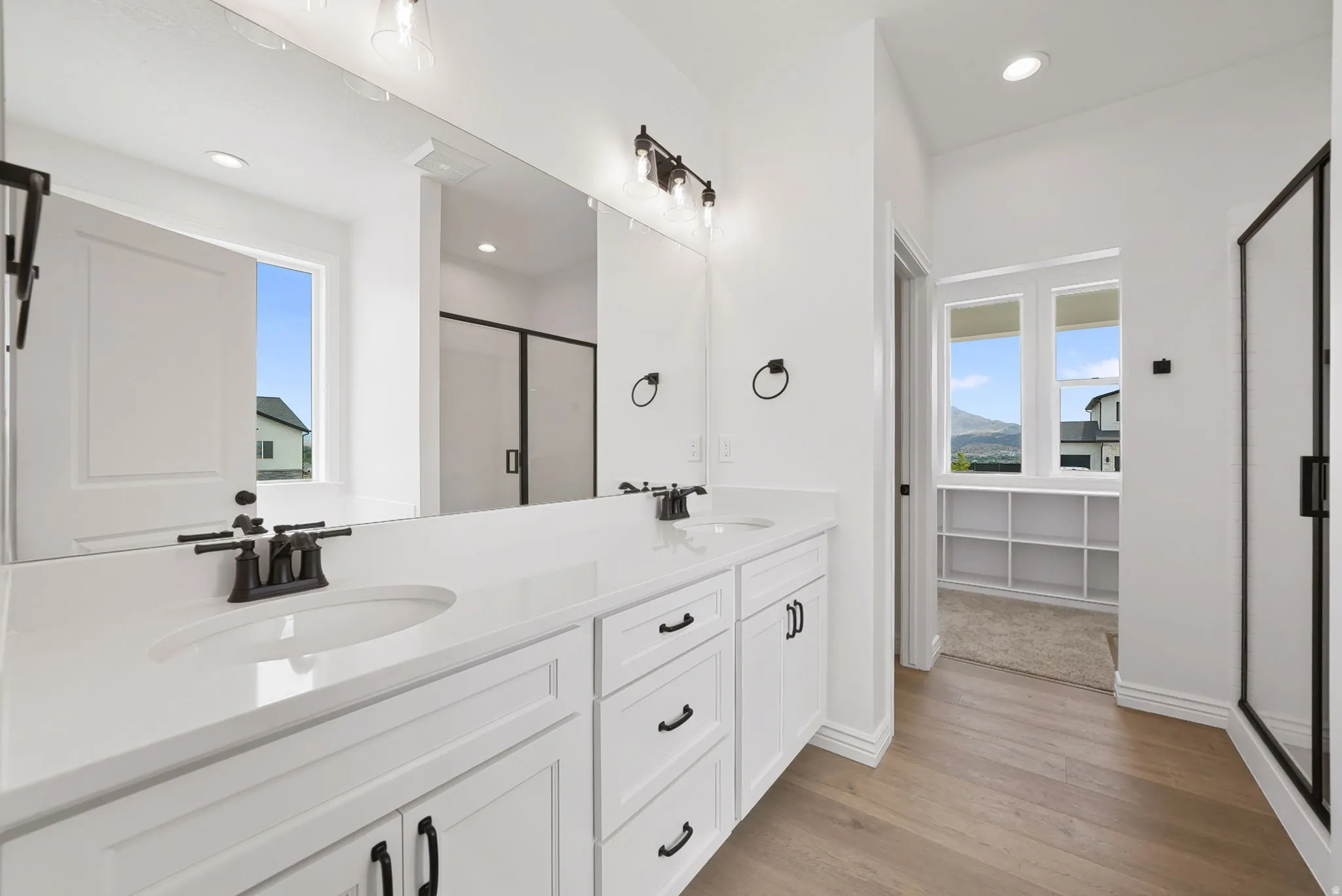 Dual vanity with white cabinetry, matte black hardware, and an expansive mirror