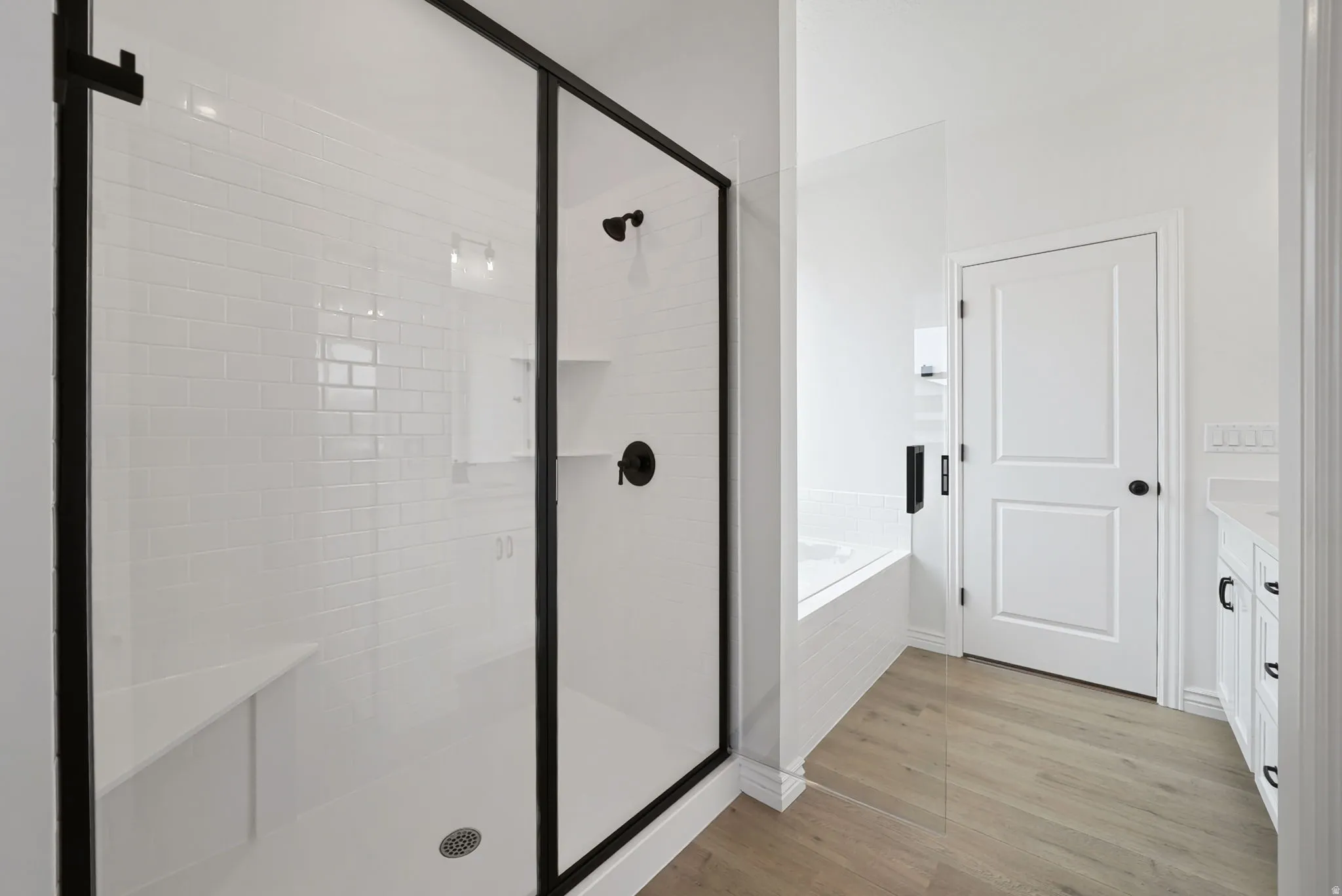 Walk-in shower with black-framed glass enclosure, white subway tile surround, integrated bench, and matte black fixtures