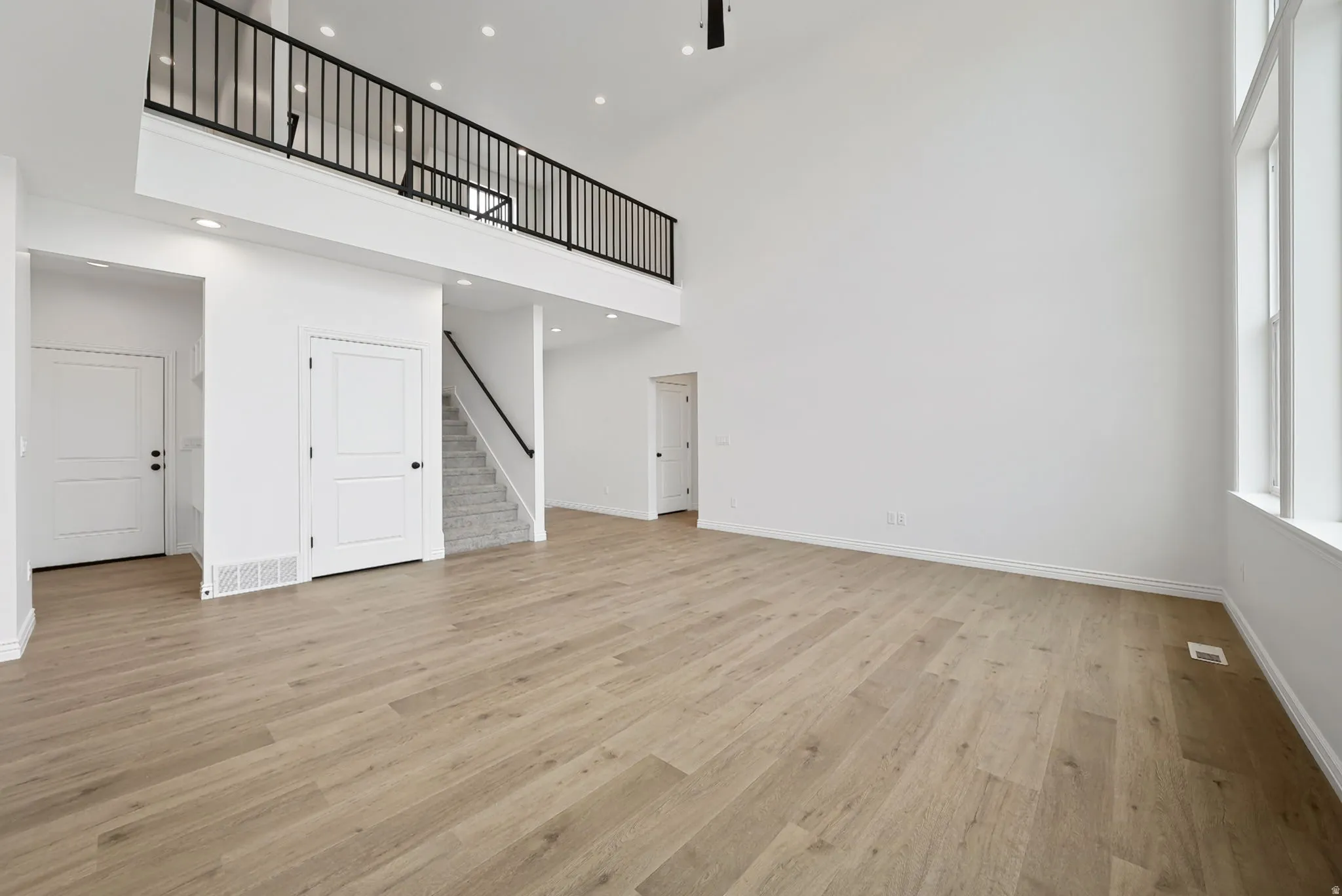 Two-story living area with high ceilings, light wood-finish flooring, and bright white walls