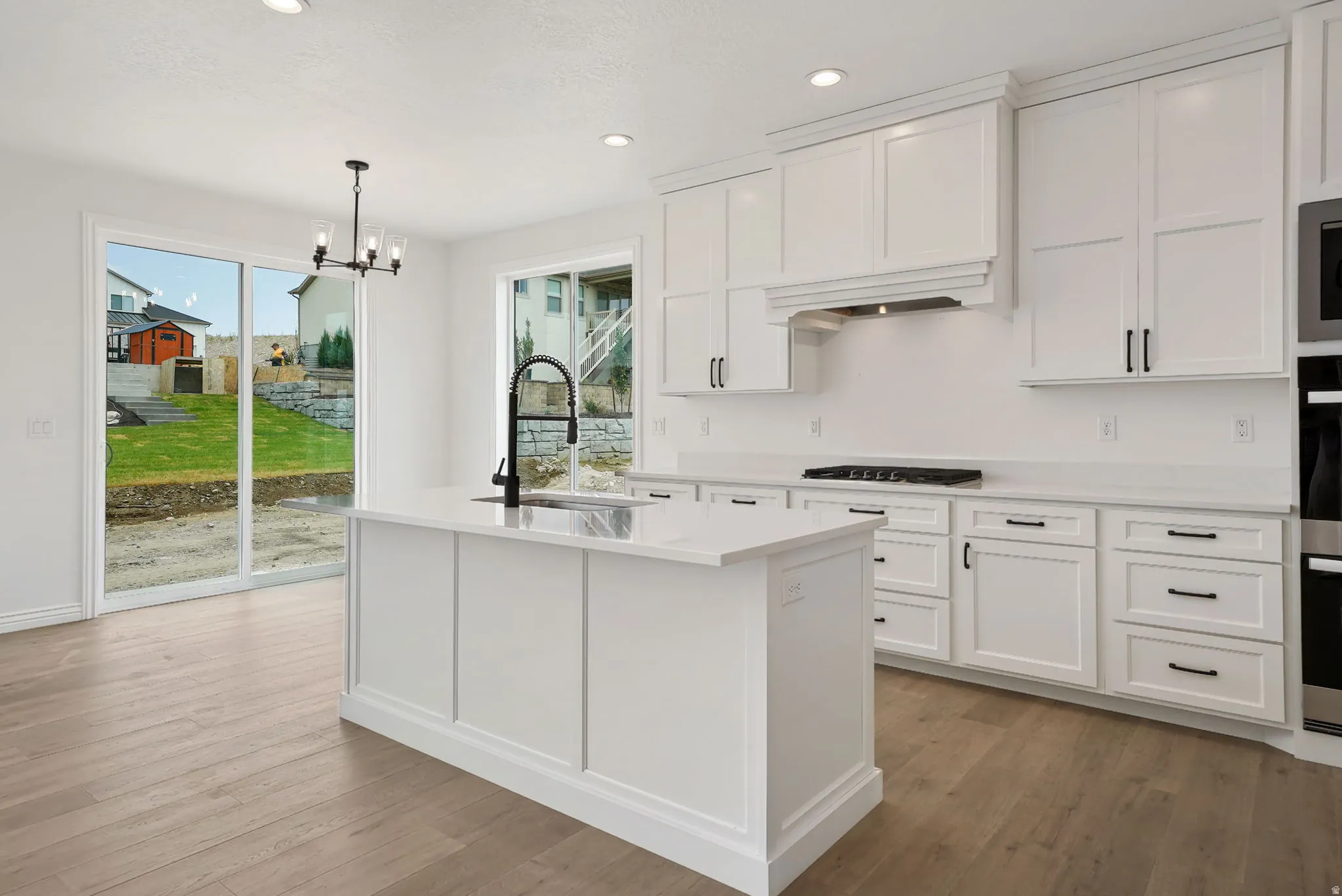 Modern kitchen featuring a central island with a sink, white shaker-style cabinetry, coordinating countertops, and wood-finish flooring