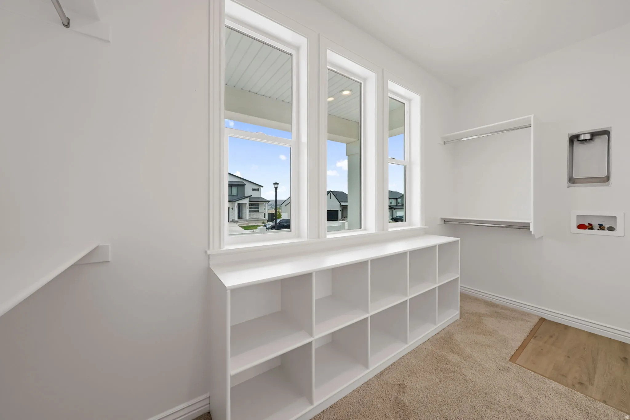 Room featuring a built-in shelving unit, three large windows with white trim, and a wall-mounted clothing rod