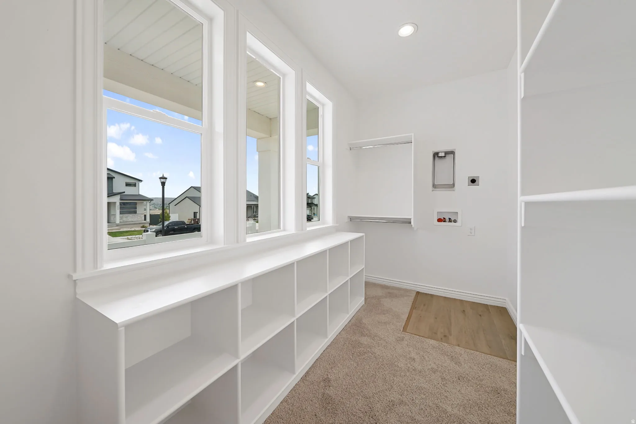 Bright utility room featuring three large windows, extensive built-in shelving, a dedicated laundry hookup area, carpeted flooring, and a recessed ceiling light