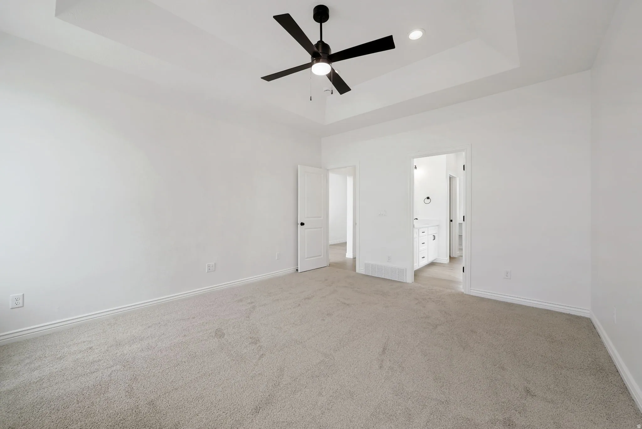 Spacious room featuring vaulted ceilings with a ceiling fan, plush carpeting, and crisp white walls