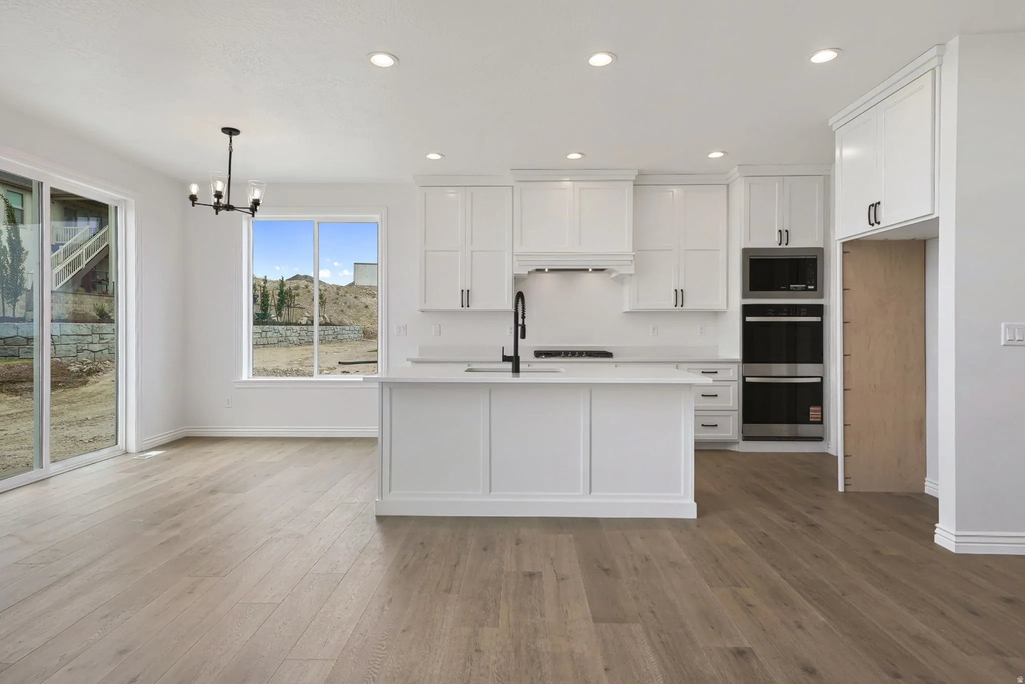 Spacious kitchen featuring white cabinetry, a center island with sink, stainless steel appliances, and wood-finish flooring