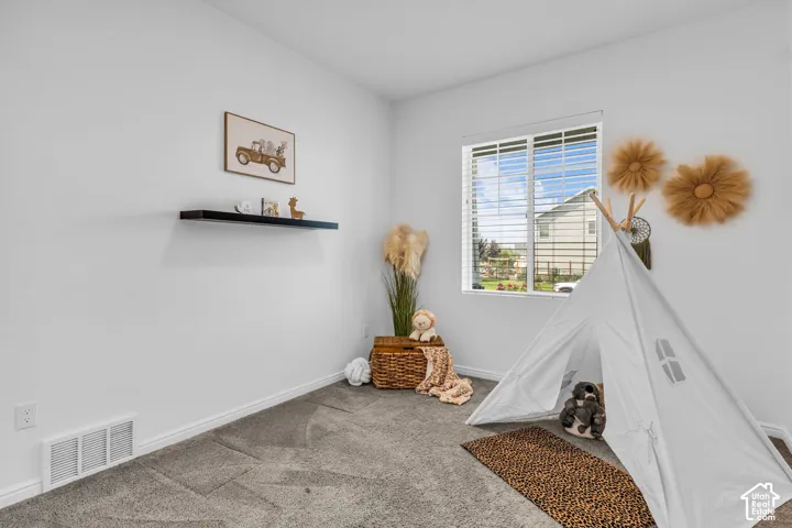 Carpeted room featuring a window with horizontal blinds, a floating black wall shelf, and white walls