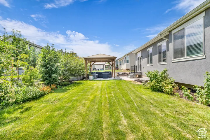 Expansive backyard featuring a manicured lawn, a built-in wooden gazebo, mature landscaping, and a concrete patio