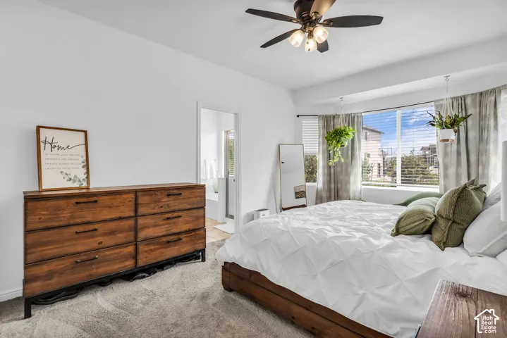 Bright bedroom featuring a large bay window, ceiling fan with integrated lighting, and a doorway opening to an additional space