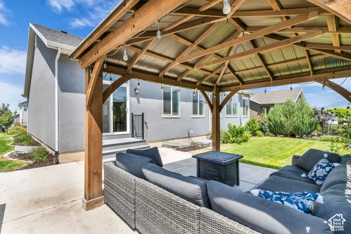 Outdoor patio featuring a wood-frame gazebo with a corrugated metal roof, string lighting, and a concrete surface