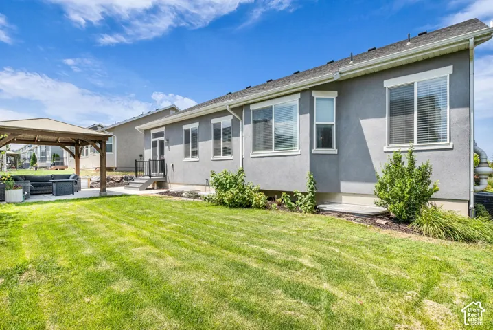 Expansive grassy yard area featuring a concrete patio with a wooden gazebo structure, a rear exterior door, and multiple windows
