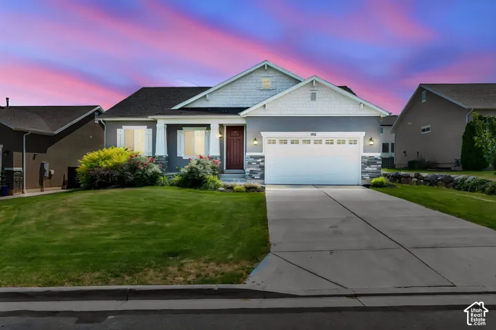 Single-story residence featuring a two-car garage, grey siding, stone accents, a dark wood-finish front door, and a concrete driveway