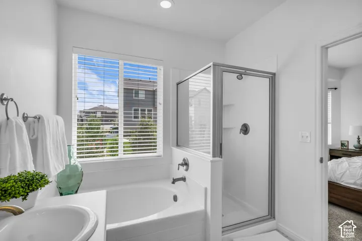Bathroom featuring a built-in tub, a glass-enclosed shower with a dark bronze fixture, and a window with horizontal blinds