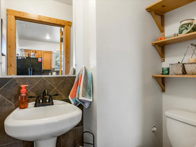 Pedestal sink with oil-rubbed bronze faucet, dark tiled backsplash, wood-finish mirror frame, and built-in wood shelving