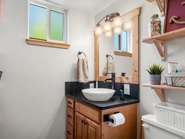 Vanity featuring a vessel sink with a matte black faucet, dark countertop, and wood cabinetry
