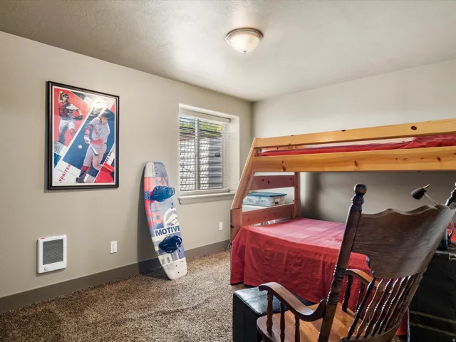 Carpeted room featuring a window with blinds, a wall-mounted heater, and a flush-mount ceiling light fixture