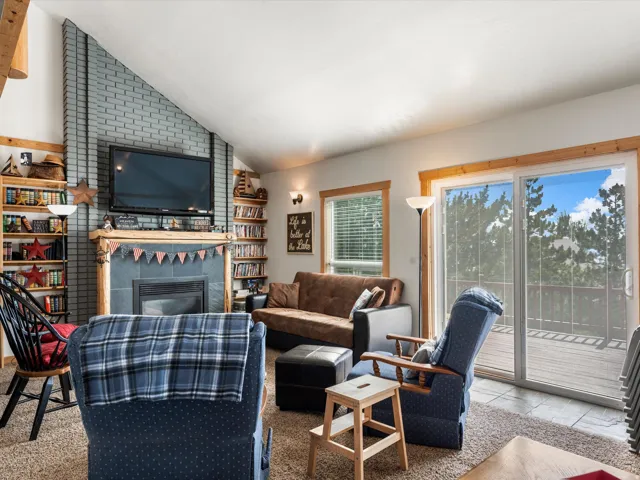 Living area featuring a floor-to-ceiling brick fireplace with a wood mantel, built-in shelving, wood-trim windows, and sliding glass doors opening to an exterior deck