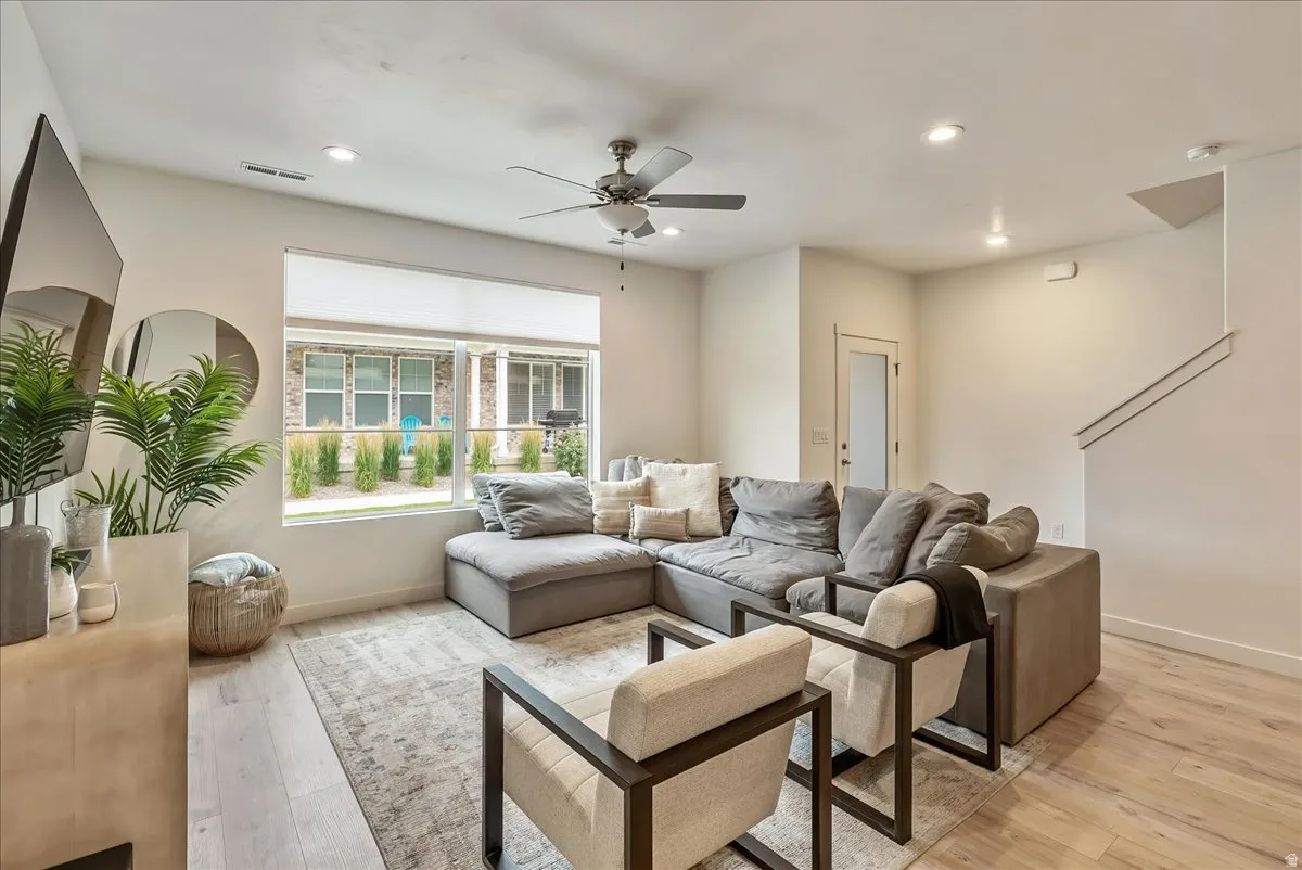 Spacious living area featuring large windows, light wood-finish flooring, recessed lighting, a ceiling fan, and a staircase