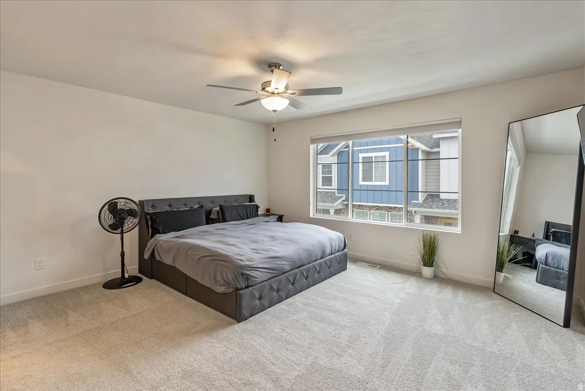 Bright bedroom featuring light-toned carpeting and a wide window with blinds