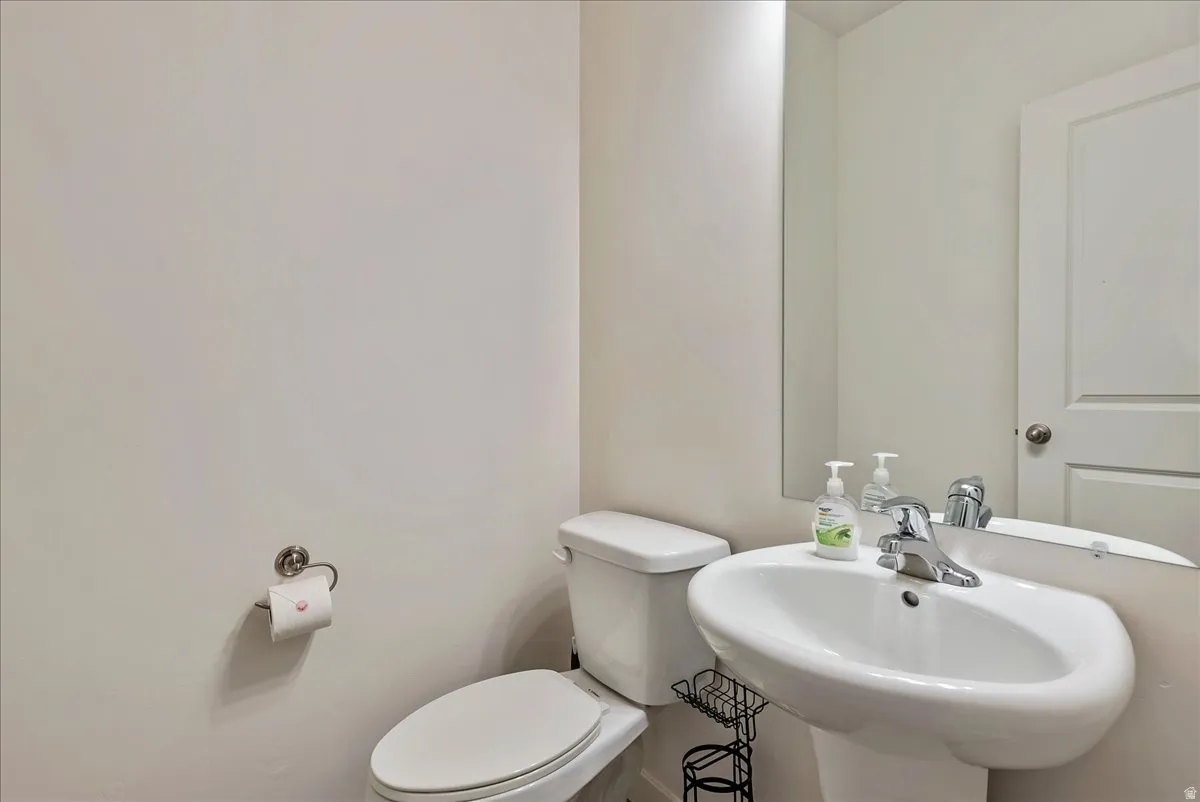Pedestal sink with chrome faucet, a wall-mounted mirror, and a white toilet