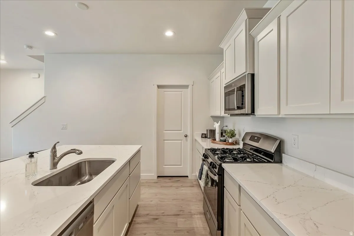Modern kitchen featuring white shaker cabinetry, stainless steel appliances, light wood-finish flooring, and white countertops with subtle veining