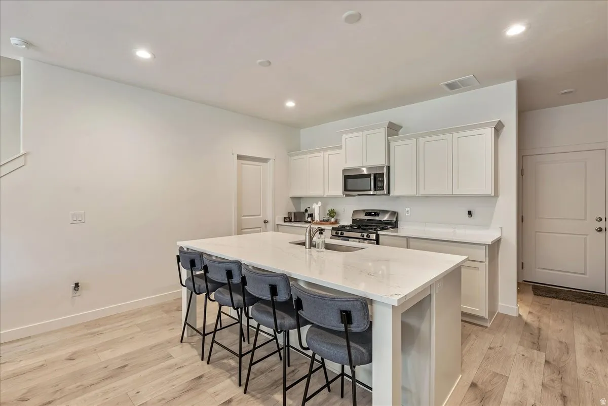 Modern kitchen featuring a large central island with seating, stainless steel appliances, light-toned cabinetry, light wood-finish flooring, and recessed lighting