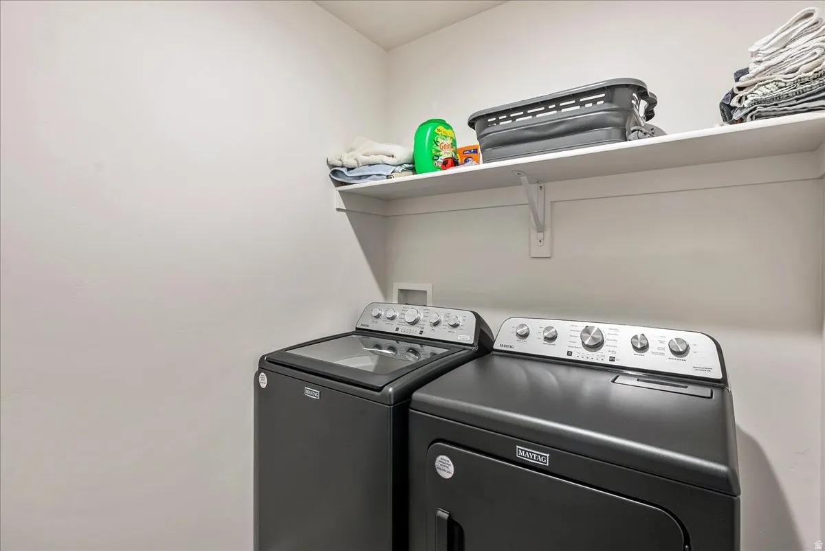 Dedicated laundry area featuring a washer and dryer set, white wall shelving, and light-toned wall finishes