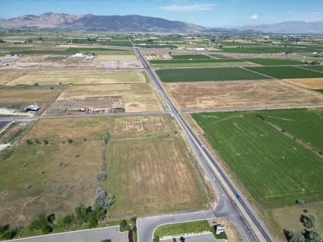 Expansive agricultural land featuring a paved road traversing multiple fields, bordered by distant mountains