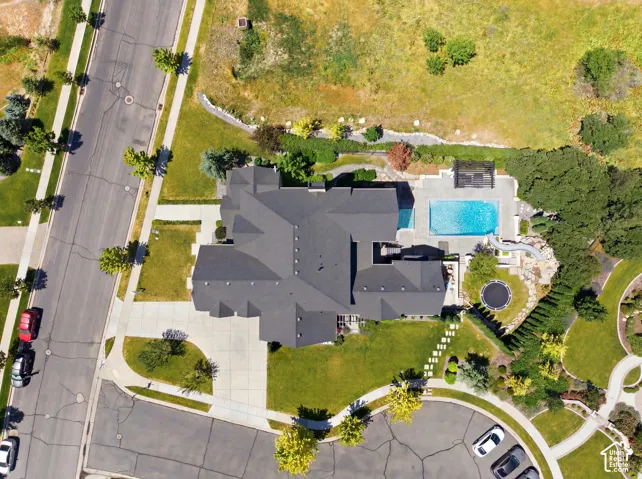 Spacious residential property featuring a dark-toned multi-gabled roofline, an expansive concrete driveway, and a large inground swimming pool with surrounding patio