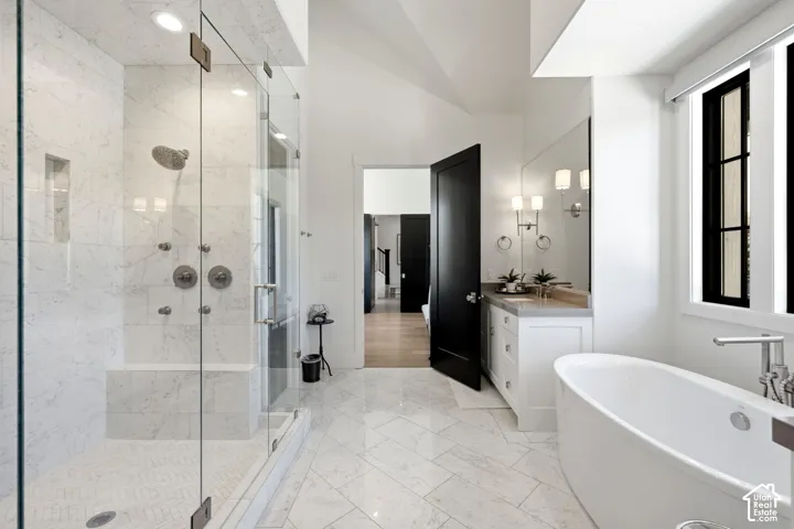 Spacious bathroom featuring a freestanding soaking tub, a large glass-enclosed shower with multiple showerheads, dual vanity with a light-toned countertop, and recessed lighting
