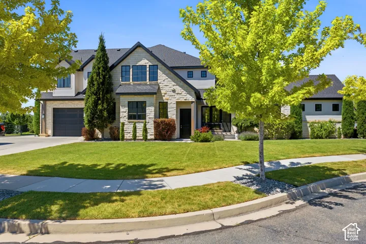 Two-story residence featuring stone and stucco exterior finishes, a dark shingle roof, and multiple large windows