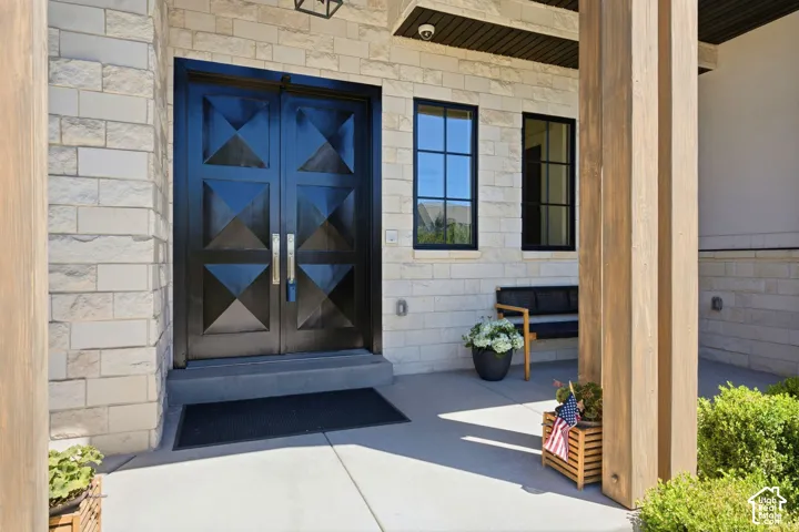 Entryway featuring dual black paneled doors with geometric detailing, stone veneer siding, and a concrete porch