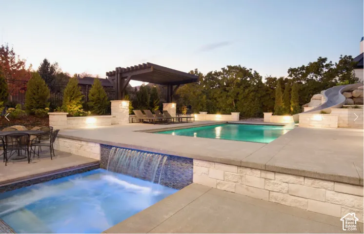 Outdoor oasis featuring a swimming pool, integrated hot tub with waterfall, and a dark wood pergola