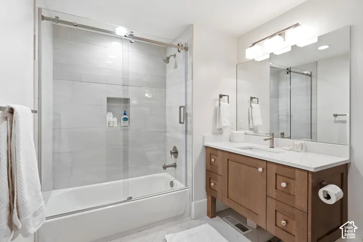 Bathroom featuring a glass-enclosed tub and shower combination with light-colored tile surround and built-in niche