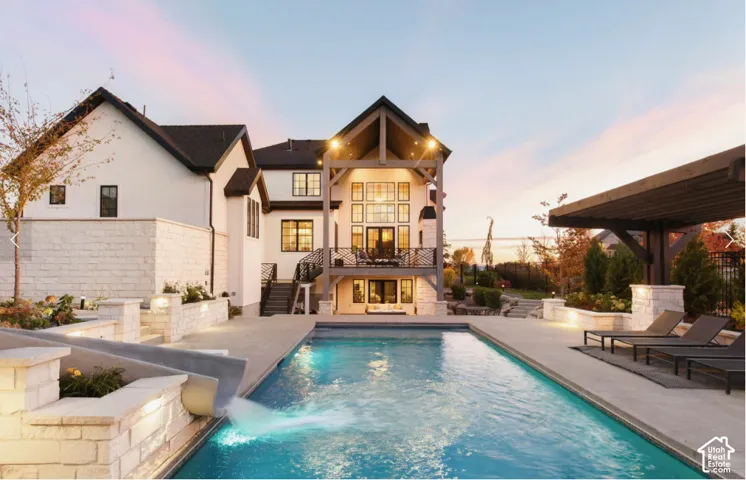 Expansive backyard featuring a rectangular swimming pool with a built-in slide, extensive stone hardscaping, a multi-level patio, and a dedicated pergola structure